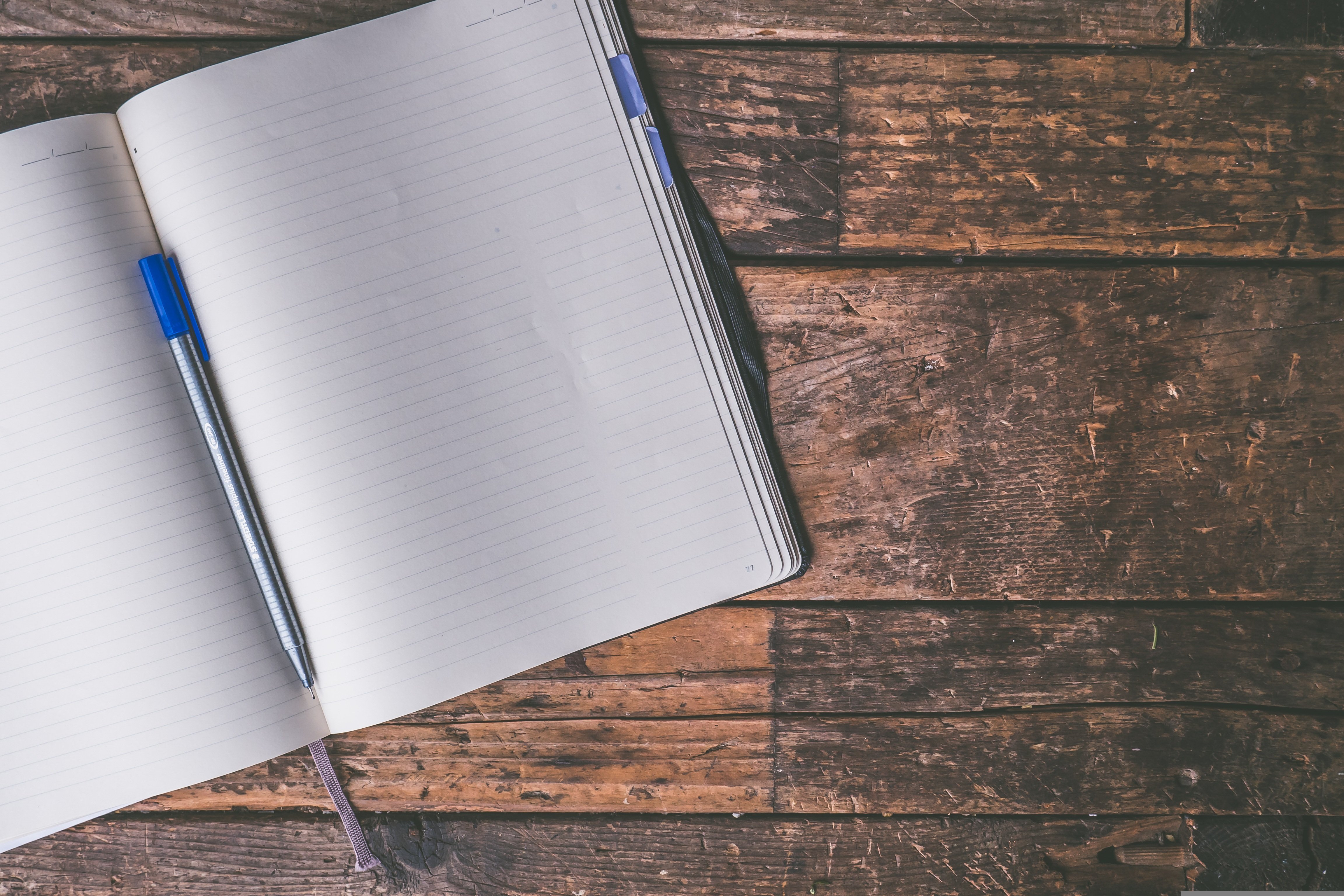 An open lined notebook with a blue pen on a worn wooden desk
